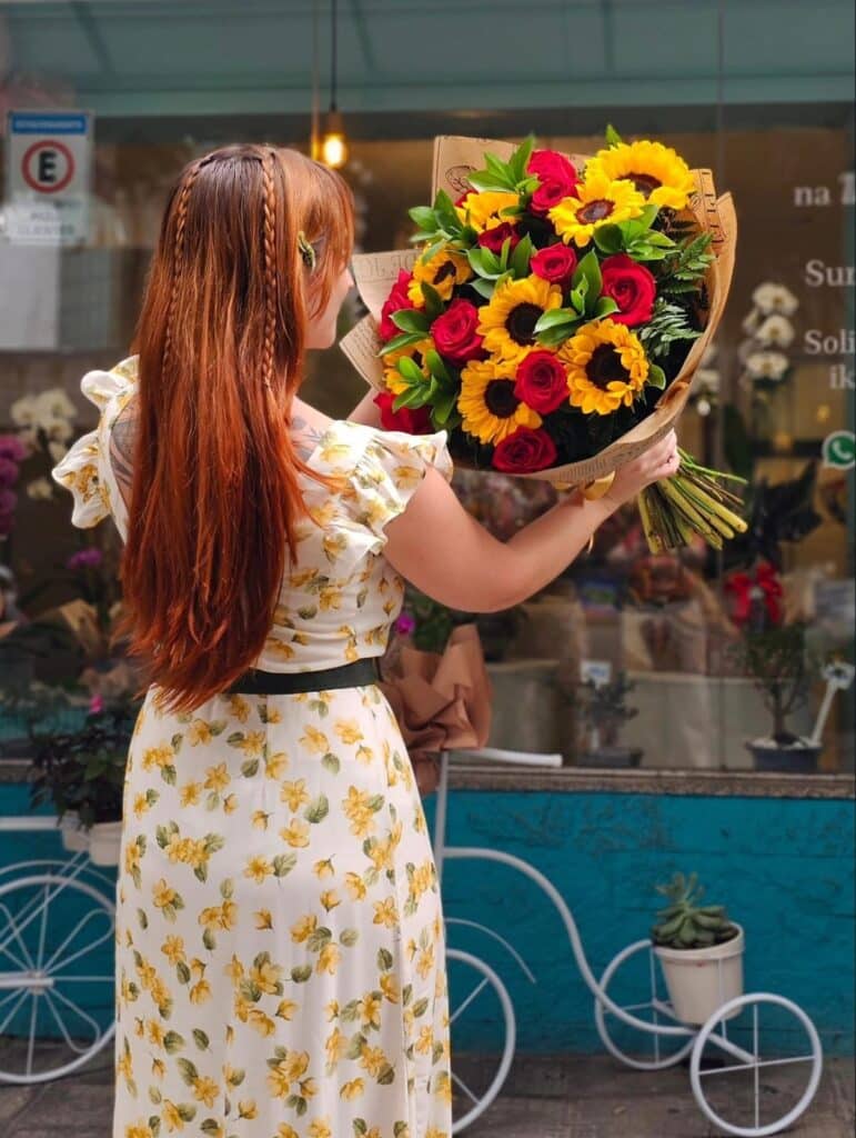 Buquê de girassóis com rosas vermelhas em frente à floricultura, arranjo vibrante para presentear