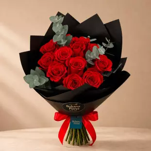 Buquê Rubi com rosas vermelhas premium, ramos de eucalipto e embalagem de papel fosco preto com laço de cetim vermelho e etiqueta oval da Ikebana Flores BH.