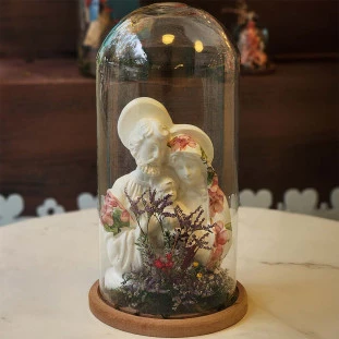 Estátua da Sagrada Família em porcelana dentro de uma cúpula de vidro decorada com flores secas