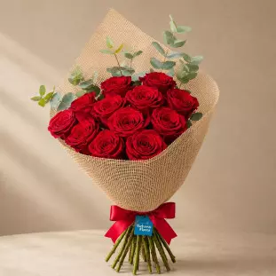 Buquê clássico com 12 rosas vermelhas premium e ramos de eucalipto, envolto em tecido rústico de juta natural com laço de cetim vermelho - Ikebana Flores BH.