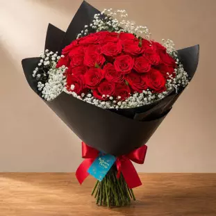buquê de rosas vermelhas envolto em um papel cartonado preto e finalizado com laço vermelho