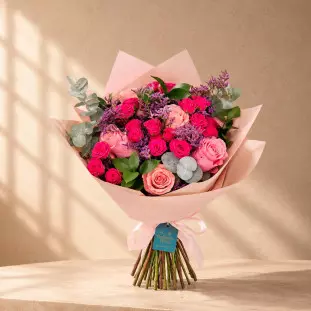 Close de buquê sofisticado contendo 5 rosas rosa pastel, 5 hastes de mini rosas vibrantes e eucalipto segurado por uma pessoa - Ikebana Flores.