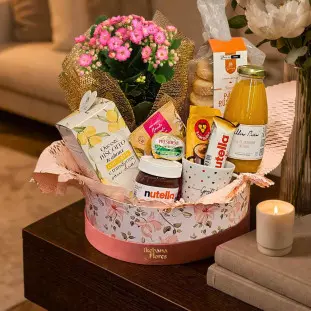 cesta de madeira repleta de produtos de café da manhã e um arranjo de kalandiva finalizada com laço rosa