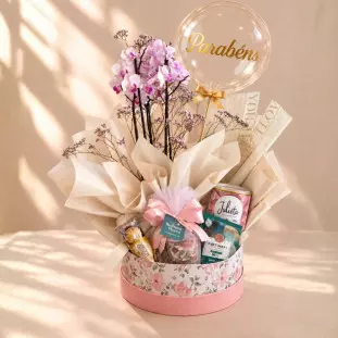 Cesta Parabéns com mini orquídea, balão bubble, Ferrero Rocher, café, biscoitos e caneca em box floral