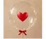 Balão transparente arredondado com coração vermelho central, laço vermelho e fitas douradas na base