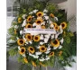 coroa de flores composta principalmente por girassóis e flores brancas menores