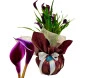 Vaso de callas roxas elegantes, envolto em papel decorativo marrom e rede dourada, com fita branca e tag azul da Ikebana Flores, perfeito para decoração ou presente especial.